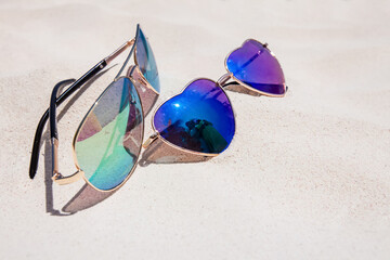 Fototapeta na wymiar Pair on sunglasses laying on the sand on sunny day. Male and female sunglasses. Heart shaped glasses. Vacation concept. Vacations on tropical island, unity concept