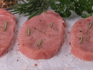Raw steak with rosemary and herbs in the background lies on white crumpled parchment paper, side view close-up.