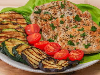 pork steak with grilled vegetables on a plate on a wooden table, closeup in a rustic style.