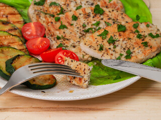 
pork steak with grilled vegetables on a plate with a knife and fork in the process of eating on a wooden table, closeup in a rustic style.