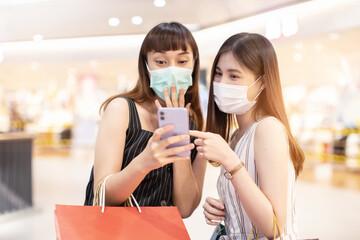 Asian woman wearing face mask. Happy woman with shopping bags enjoying in shopping. Girl holding colour paper bag.Friends walking in shopping mall.time shopping coronavirus crisis or covid19 outbreak