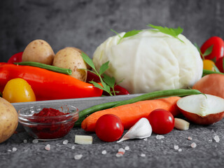 
vegetables and greens in a gray wooden diagonal tray on a stone background, closeup.