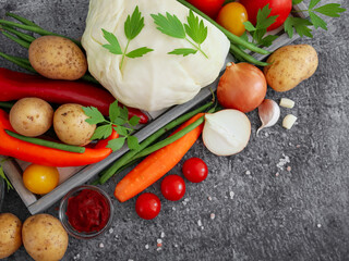 vegetables and greens in a gray wooden diagonal tray on a stone background, with place for text in the lower left corner, top view close-up.