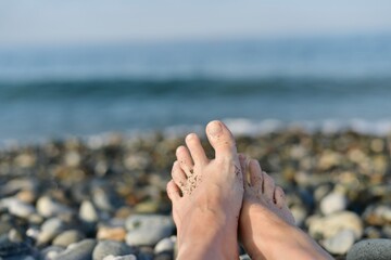 Two bare feet, slightly folded into a hug, against the sea is out of focus.