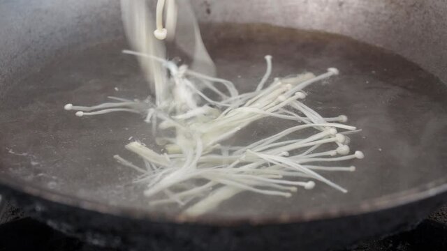 Chef droping enoki mushrooms in boiling water