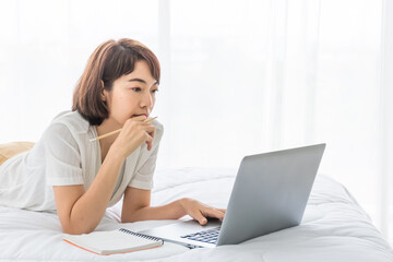 asian business woman work from home via laptop on bed with notebook.