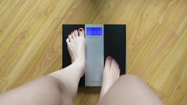 A woman gets on the scales and sees her weight at kilograms. The girl is cunning and pushes off the floor to reduce the figure. First-person view. Comic image of a losing weight woman