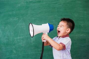 Back to School. Asian funny cute little child boy kindergarten preschool in student uniform speaking through megaphone against on green school blackboard, First time to school education concept