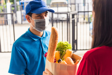 Asian young delivery man in uniform wear protective face mask he making grocery service giving...
