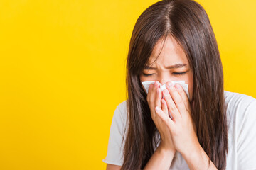 Portrait of Asian beautiful young woman sad she crying wipe the mucus with tissue, Close up of pretty girl sneezing sinus using towel to wipe snot from nose, studio shot isolated on yellow background