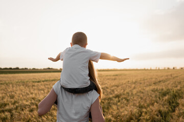 very happy family of mother and son having fun outdoors at summer sunset. The child sits on his...