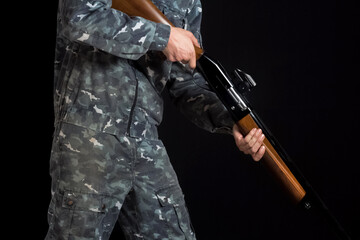 Soldier, trooper on a black background. A man with a gun in camouflage military uniform. Military or hunter with a shotgun. A man holding a gun with a sight. Man in army uniform.
