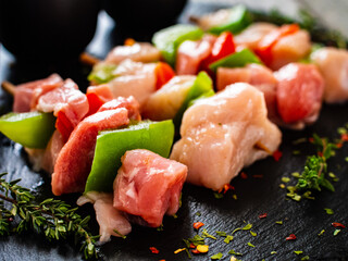 Uncooked shashlik and seasonings on black stone board on wooden table