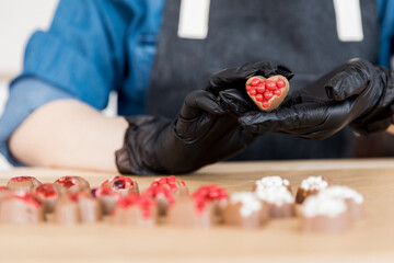 Close-up heart-shaped chocolates with red filling in hands of confectioner woman on kitchen...