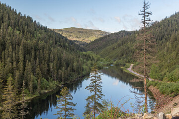 Landscape with a beautiful mountain lake among the mountains covered with coniferous and deciduous trees.