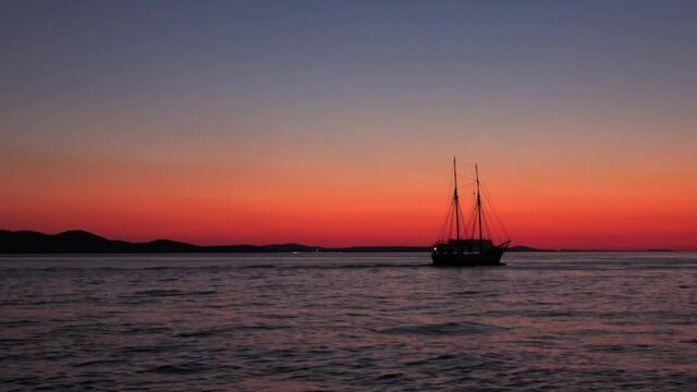 Romantic sunset at Zadar, Croatia. With a warm gradient of vivid colours in the clear sky and its reflection in the calm waters, while a two-masted old-style ship passes by.
