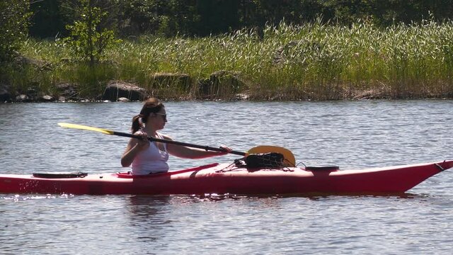 Woman rowing red kayak in clean Scandinavian nature on a sunny summer day, slow motion