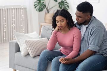 Caring Afro Man Comforting His Depressed Wife At Home, Embracing And Supporting