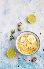 Homemade chicken bouillon or broth with noodle and egg served with thyme and lime on blue stone background. Top view.