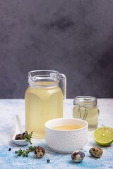 Homemade chicken or vegetable bouillon or broth in bowl and glass storage jars on blue concrete background.