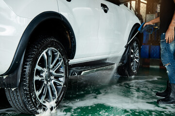 Manual Car Wash. Man using High Pressure Water Machine and Soap to Cleaning Car. Focus on Wheel
