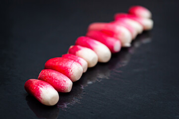 Line lined with fresh red peeled radish on a background of wet black stone