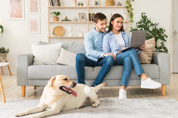Young happy couple sitting on sofa with their labrador