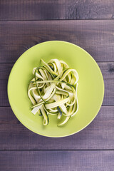 Plate with raw zucchini spaghetti on a wooden background