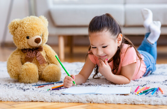 Asian Kid Girl Drawing Picture Lying On Floor At Home