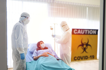 A patient woman wear face mask and cure on bed and covid-19 emergency treatment in a hospital room, doctors wear uniform protection