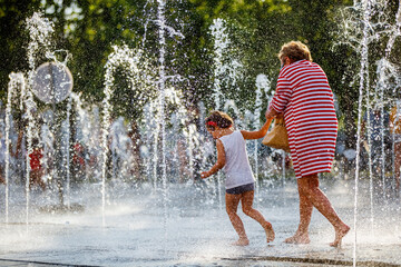 Mother with her daughter playing in the fountaine on a hot summer day
