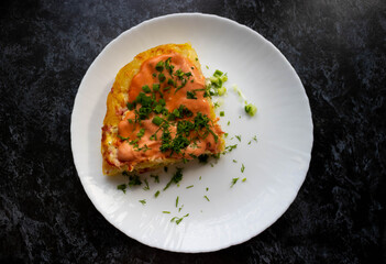 A portion of potato casserole with sauce and herbs on a white plate