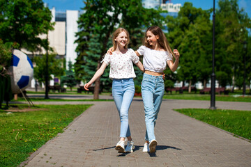 Two happy girlfriends teenagers are walking in the summer park.