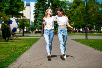 Two happy girlfriends teenagers are walking in the summer park.