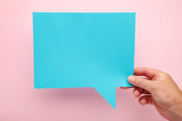 Fototapeta premium Hand holding an blue empty speech bubble on pink background