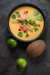 Cast-iron pan with thai-style pumpkin, coconut milk and prawn soup, vertical shot on a brown stone surface, view from above