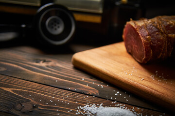 Large white smoked salt on an old black telephone cutting board on a dark wooden table close-up with shallow depth of field and blur.