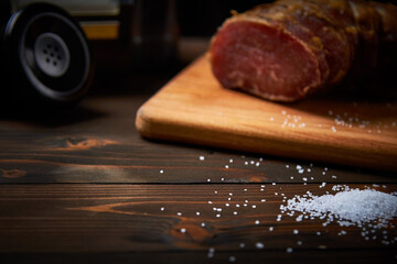 Large white smoked salt on an old black telephone cutting board on a dark wooden table close-up with shallow depth of field and blur.