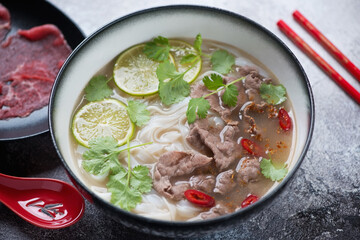 Bowl of traditional vietnamese pho bo soup over grey stone background, selective focus, studio shot