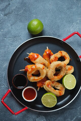 Serving pan with fried breaded calamari rings and crab claws, above view on a blue stone background, vertical shot