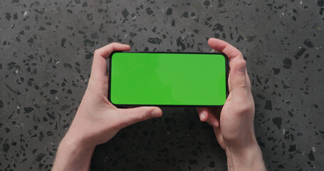 Top view man hand show smartphone with green screen on concrete background
