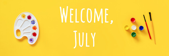 Welcome July text. Colorful flowers on artistic palette, brush, gouache on yellow background. Creative concept Hello summer. Top view Flat lay Banner