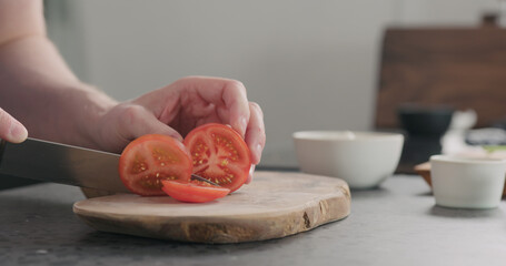man slicing tomato on olive wood board