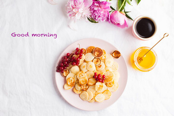 Tiny pancakes with berries, honey, flowers, coffee and the words good morning. Pancake porridge. concept of Breakfast.