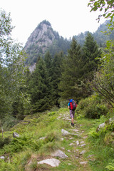 The view of a man walking on a hiking path with mountain peak on background.