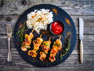 Grilled shashlik and white basmati rice on black stone plate on wooden table
