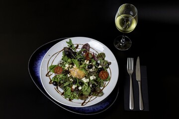 High angle shot of a plate of Greek salad and a glass of white wine on a black background