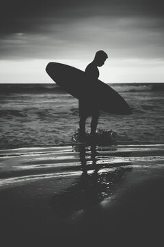 Backlit of a surfer walking along the seashore with his surfboard during the sunset