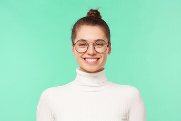Young student girl in eyeglasses and white sweater, feeling confident and smiling happily, happy with working day, isolated on mint blue background