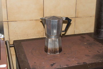 The view of big metal stovetop coffee maker on a cast iron wood burner stove.